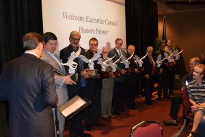 General Overseer Mark Williams, back to photo) presents awards of appreciation to outgoing Executive Council members (l-r) Kevin Wallace, David Ramirez, Bryan Cutshall, Victor Pagan, Thomas Madden, Bill Isaacs, Dwight Allen, Niko Njotorahardjo, and Chris Moody (click photo to enlarge).